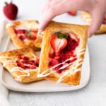 a person is holding a strawberry tart on a plate.