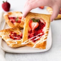 a person is holding a strawberry tart on a plate.