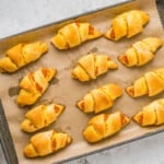 pumpkin pie crescent rolls lined up on a parchment-lined baking tray.