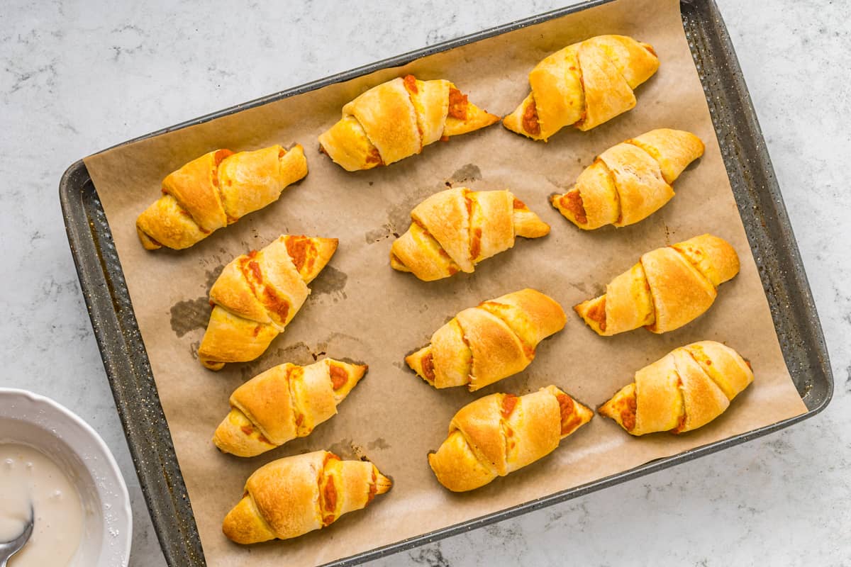 pumpkin pie crescent rolls lined up on a parchment-lined baking tray.