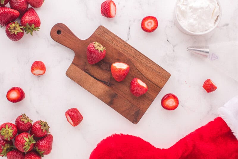 strawberries with the top sliced off are lined up on a cutting board.