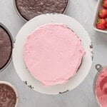 a pink cake with strawberries and icing on a white plate.