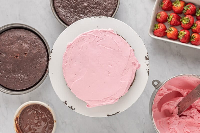 a pink cake with strawberries and icing on a white plate.