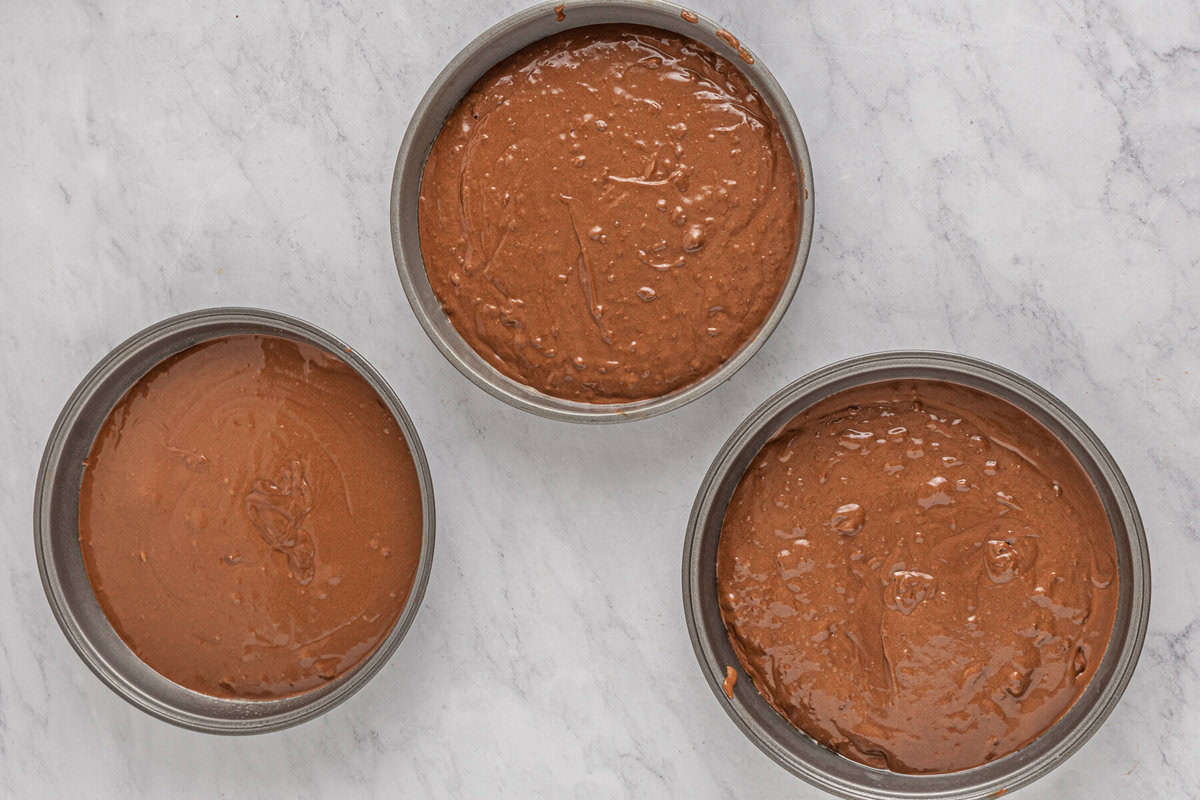 three round cake pans filled with chocolate batter.