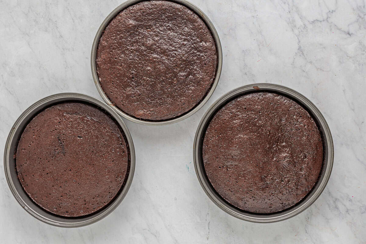 three baked chocolate cake layers in round cake pans.