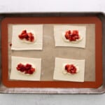 four squares of pastry with strawberries and cream on a baking sheet.