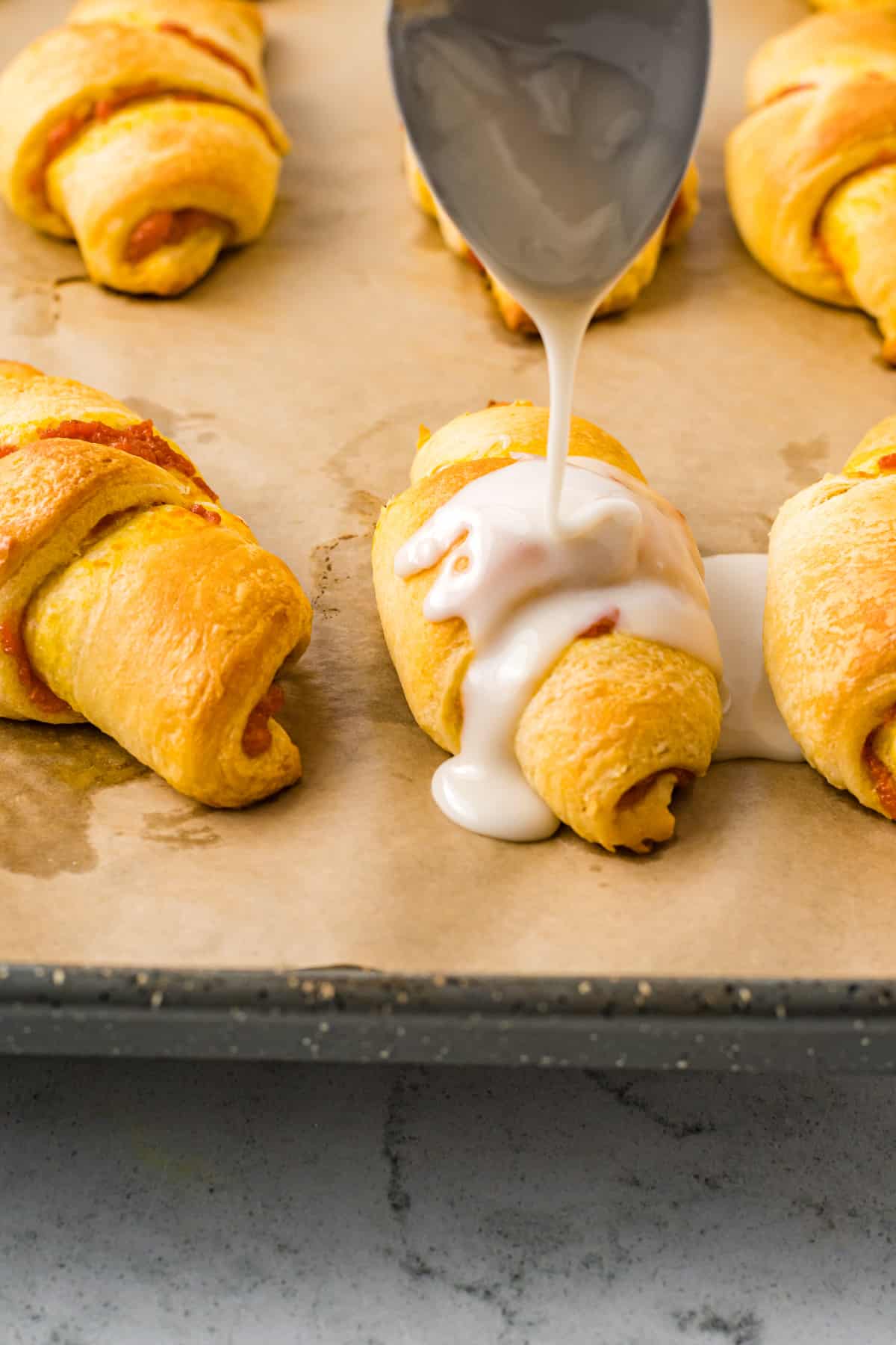 spoon drizzling icing on top of pumpkin crescent rolls