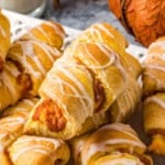 a serving tray of pumpkin pie crescent rolls is set on a table next to a glass of milk and a decorative orange pumpkin.