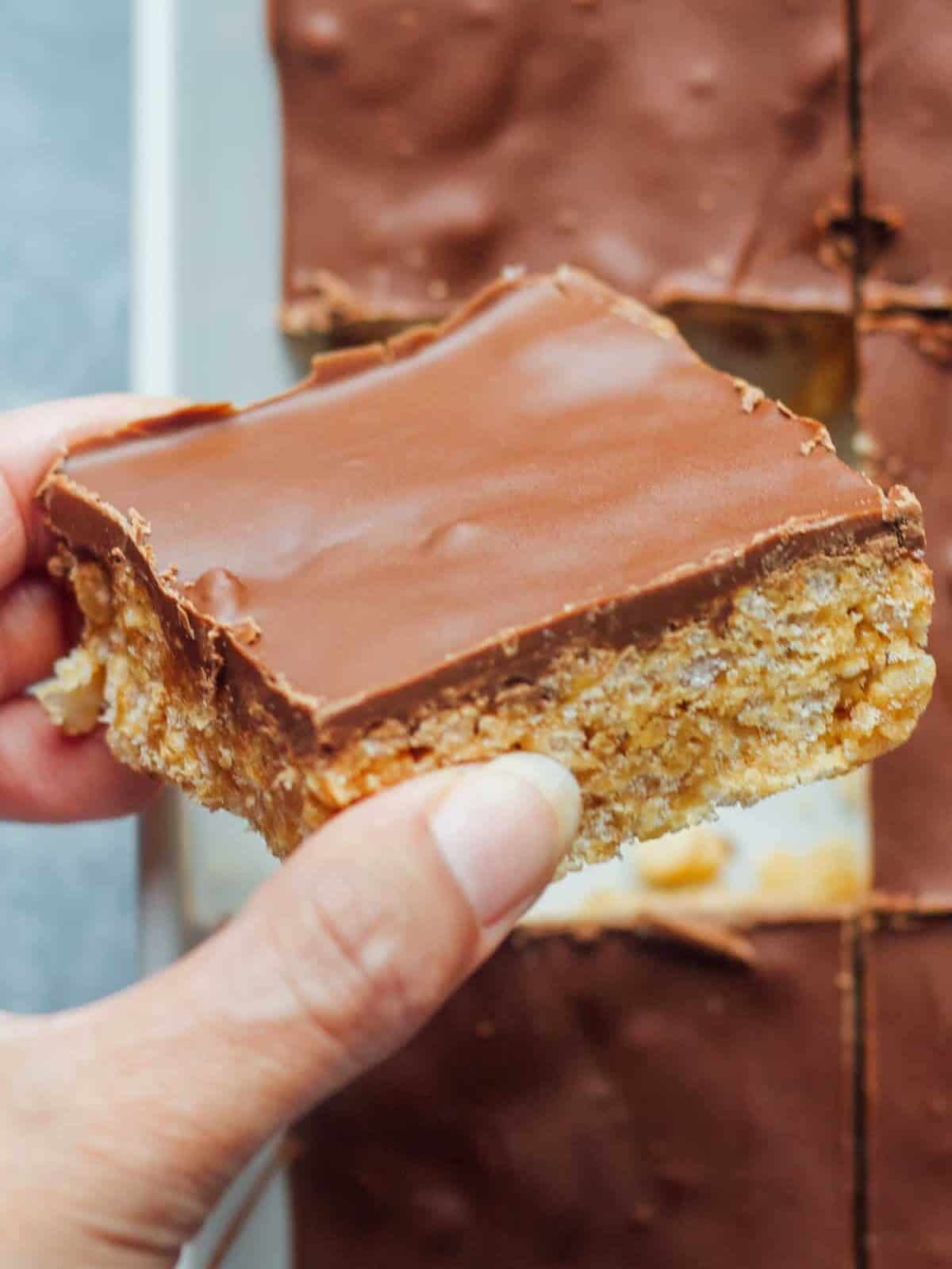 close up of a hand holding a scotcheroos bar topped with chocolate
