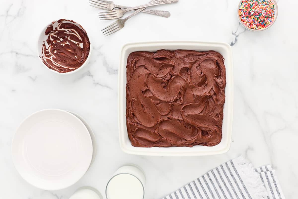 chocolate cake in a white dish with icing and sprinkles.