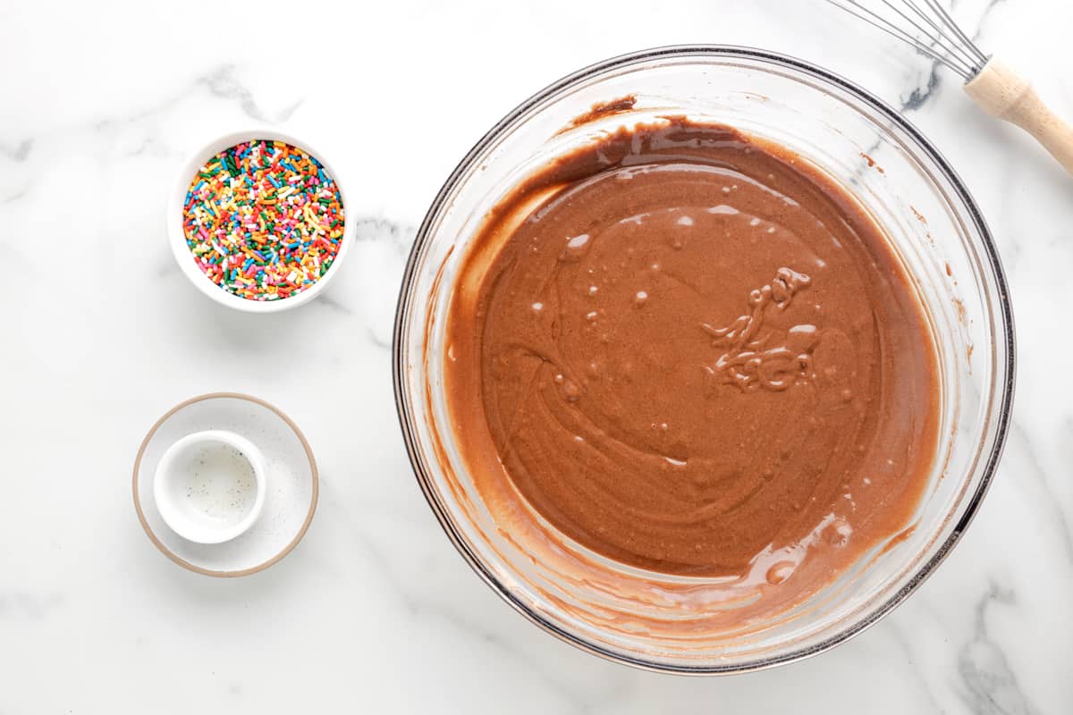 a bowl of chocolate ganache with sprinkles and a whisk.