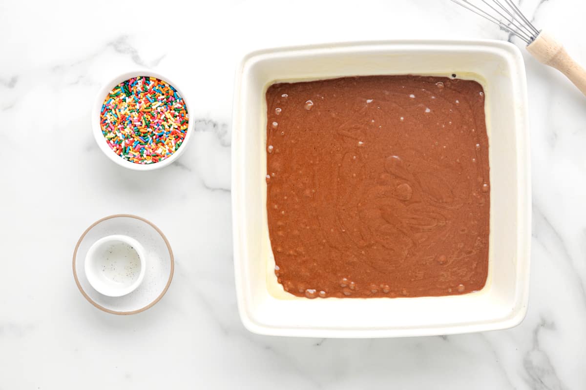 a bowl of chocolate cake with sprinkles and a whisk.