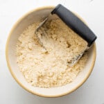 crumbled pastry dough in a white bowl with a pastry cutter.