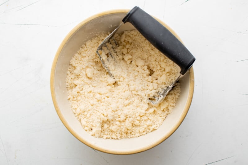 crumbled pastry dough in a white bowl with a pastry cutter.