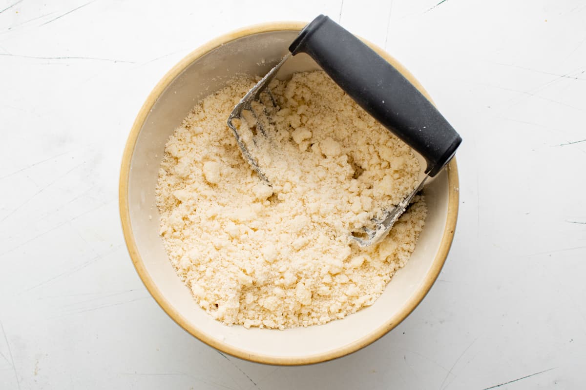 crumbled pastry dough in a white bowl with a pastry cutter.