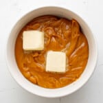melted caramel with butter pats on it in a white bowl.