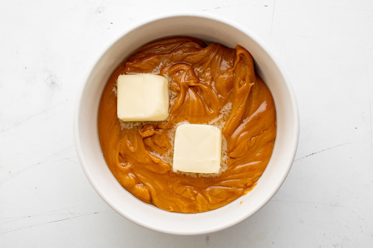 melted caramel with butter pats on it in a white bowl.