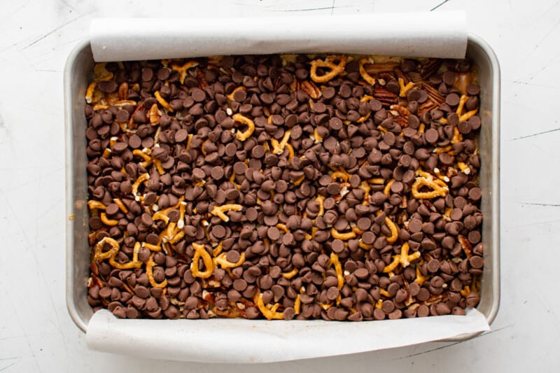chocolate chips sprinkled over turtle bars in a baking pan.