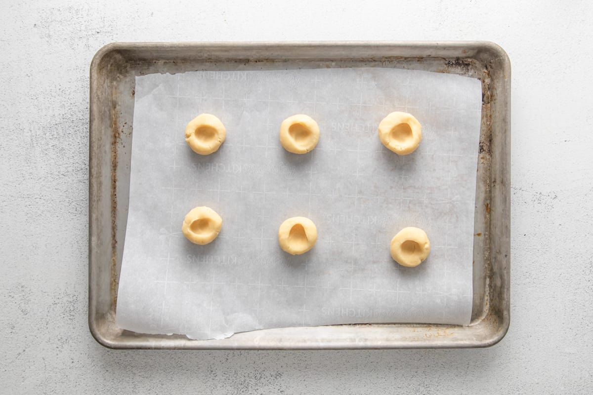 6 dimpled shortbread cookie dough balls on a baking sheet.