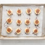 12 twix cookies on a baking sheet filled with caramel and topped with chocolate drizzle.