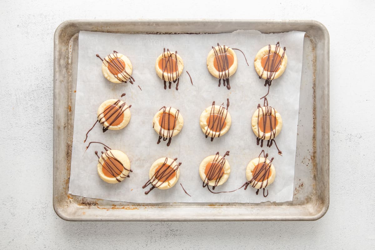 12 twix cookies on a baking sheet filled with caramel and topped with chocolate drizzle.