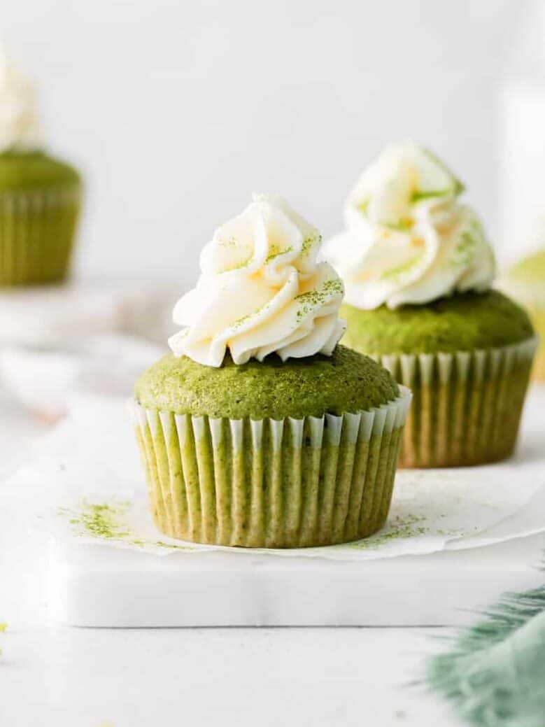 side view of 2 matcha cupcakes on parchment paper on a marble tray.