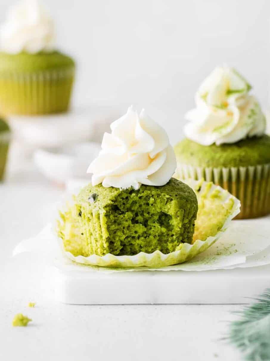 side view of 2 matcha cupcakes on parchment paper on a marble tray, one is bitten.