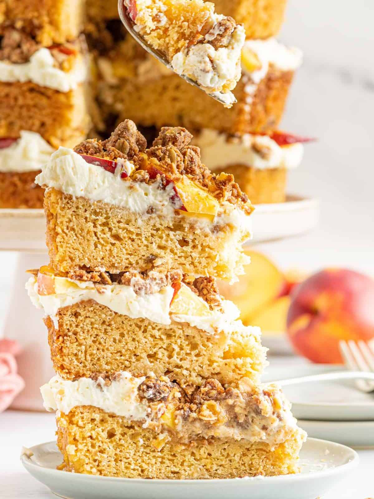 slice of triple layered peach cobbler cake on a plate, in front of a whole cake on a cake stand