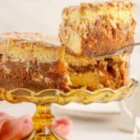 lifting a slice of peach cobbler cheesecake from the cake stand