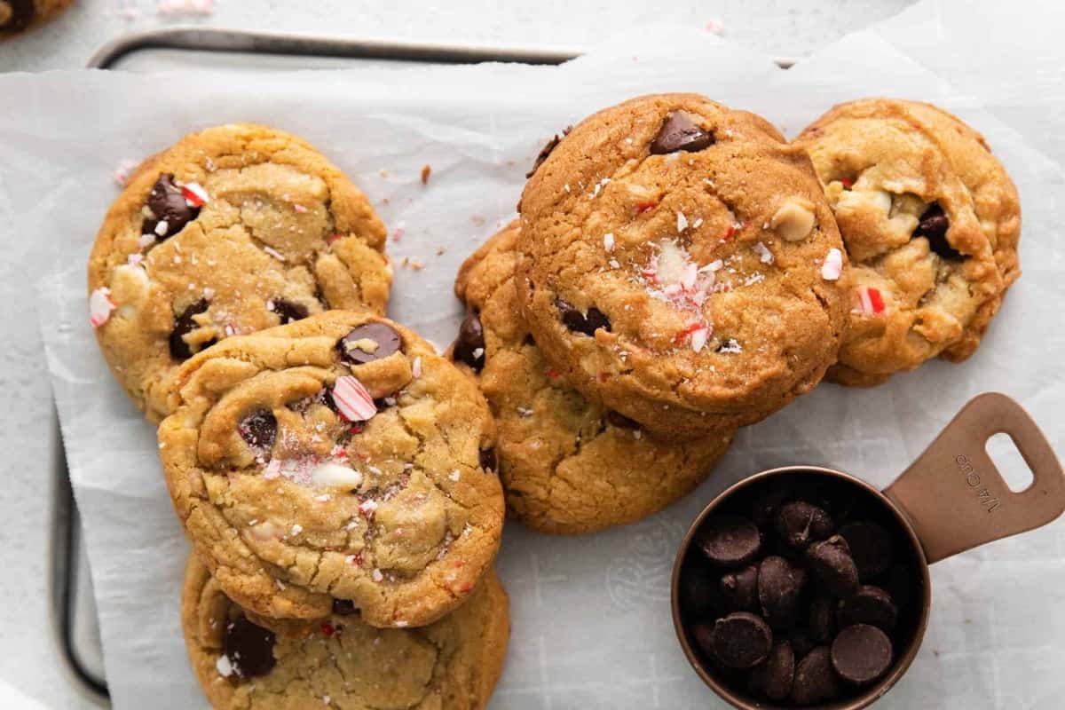 overhead view of a pile of peppermint chocolate chip cookies on a baking sheet next to a measuring cup filled with chocolate chips.
