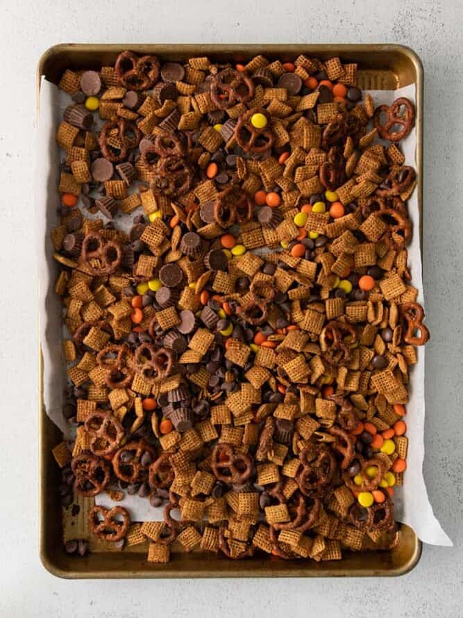 Chex mix with candies and pretzels spread out on a baking tray