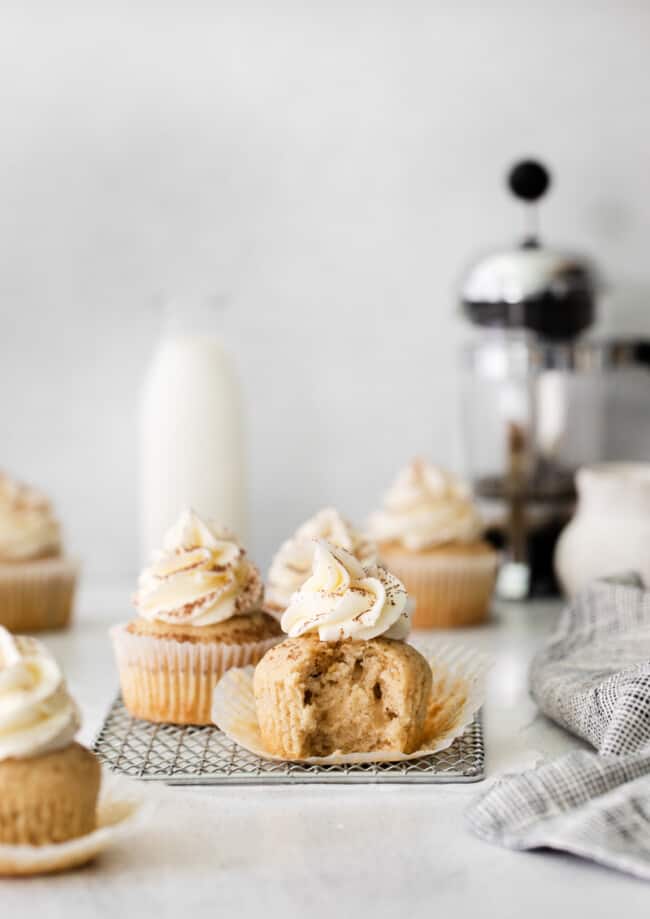 side view of an unwrapped and bitten tiramisu cupcake on a small wire rack in front of another cupcake.