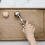 scooping cookie dough onto a baking sheet with a cookie scoop.