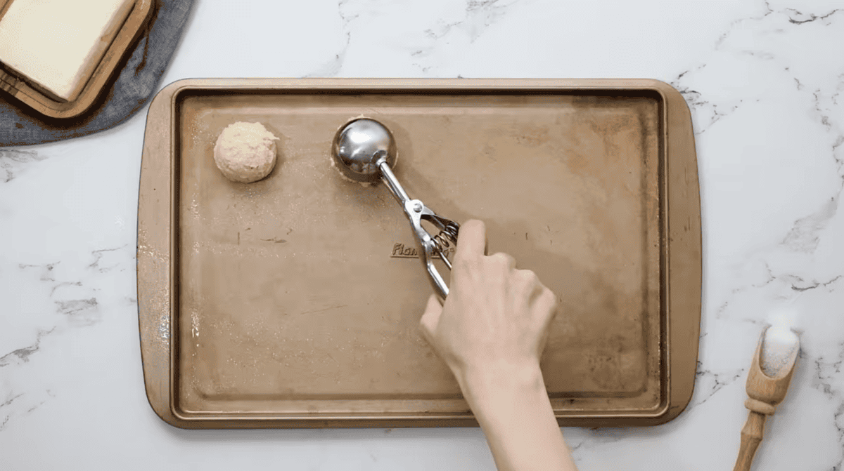 scooping cookie dough onto a baking sheet with a cookie scoop.