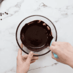 stirring chocolate glaze with a rubber spatula in a glass bowl.