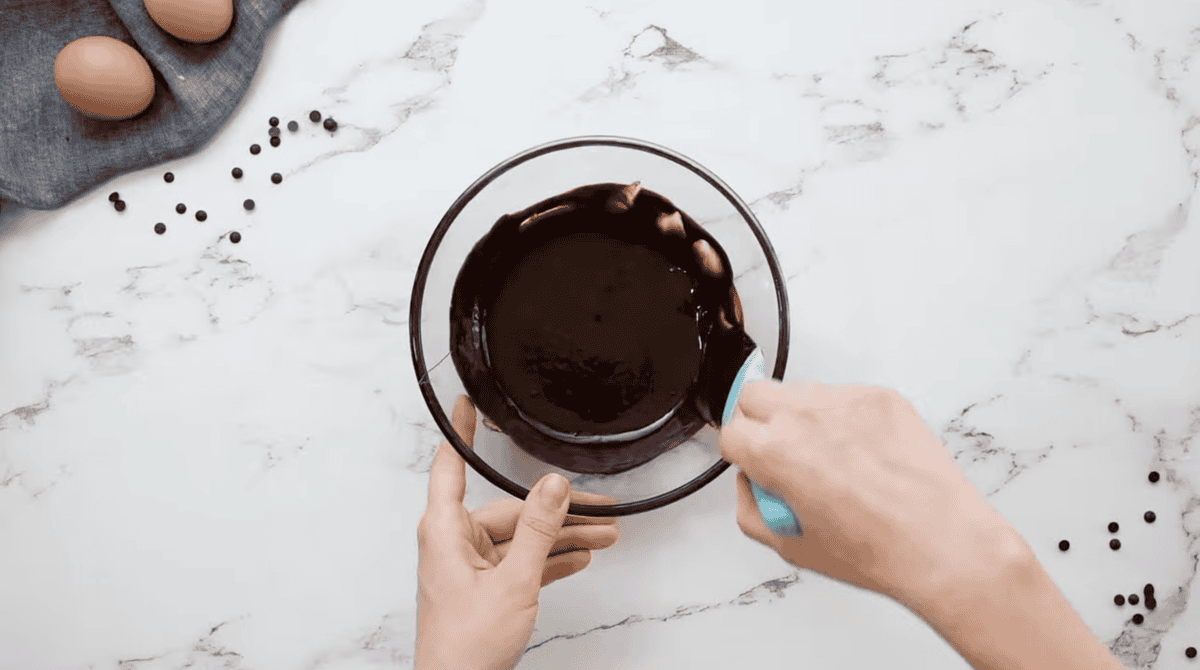 stirring chocolate glaze with a rubber spatula in a glass bowl.