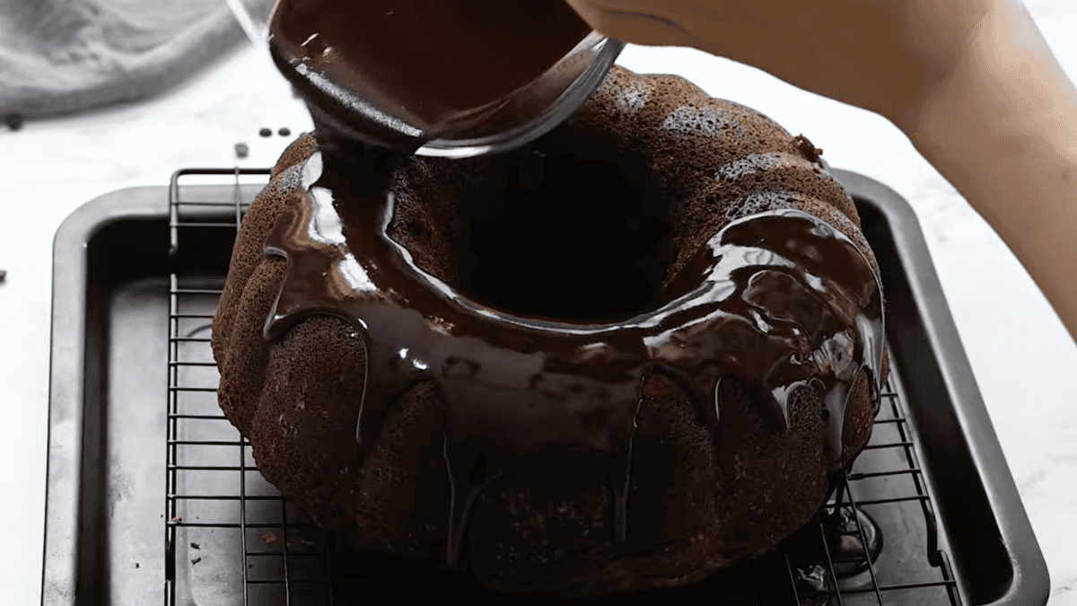 pouring chocolate glaze over chocolate pound cake on a wire rack set in a baking sheet.