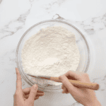 mixing flour and powdered sugar in a glass bowl with a rubber spatula.