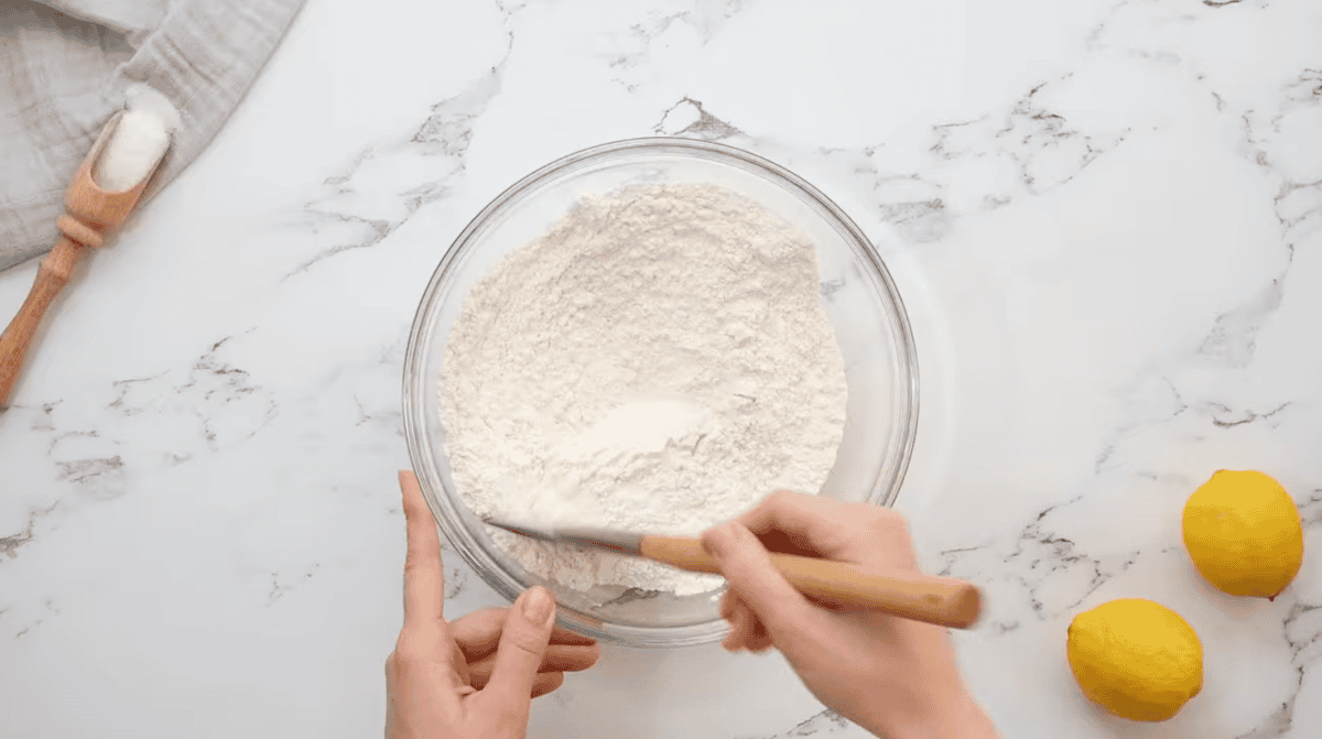 mixing flour and powdered sugar in a glass bowl with a rubber spatula.