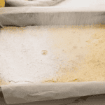 dusting baked lemon bars with powdered sugar in a baking pan.