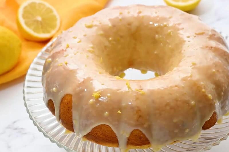lemon bundt cake with white chocolate lemon glaze and lemon zest on top of a glass cake stand.