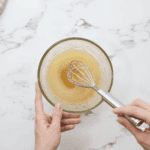 hydrated lemon jello in a glass bowl with a whisk.