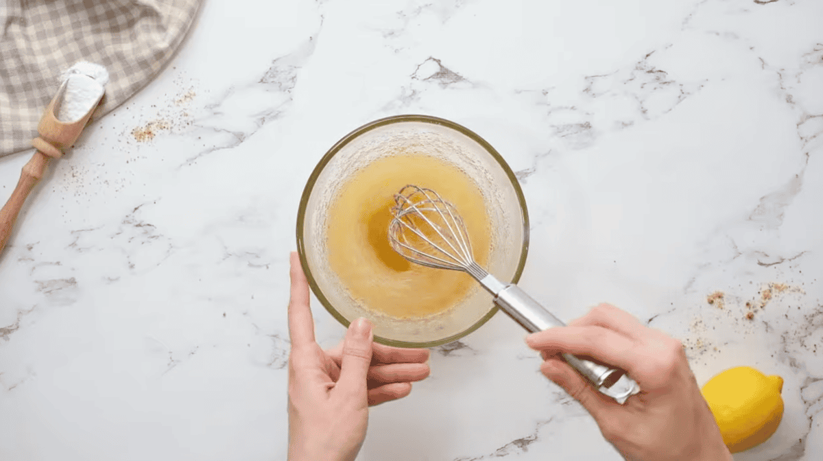 hydrated lemon jello in a glass bowl with a whisk.