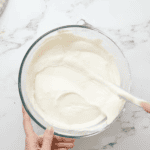 lemon flavored cheesecake filling in a glass bowl with a rubber spatula.