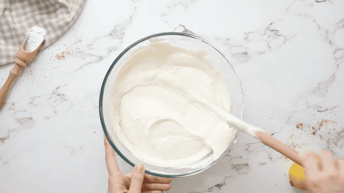 lemon flavored cheesecake filling in a glass bowl with a rubber spatula.