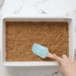 pressing graham cracker crust into a baking pan with a rubber spatula.