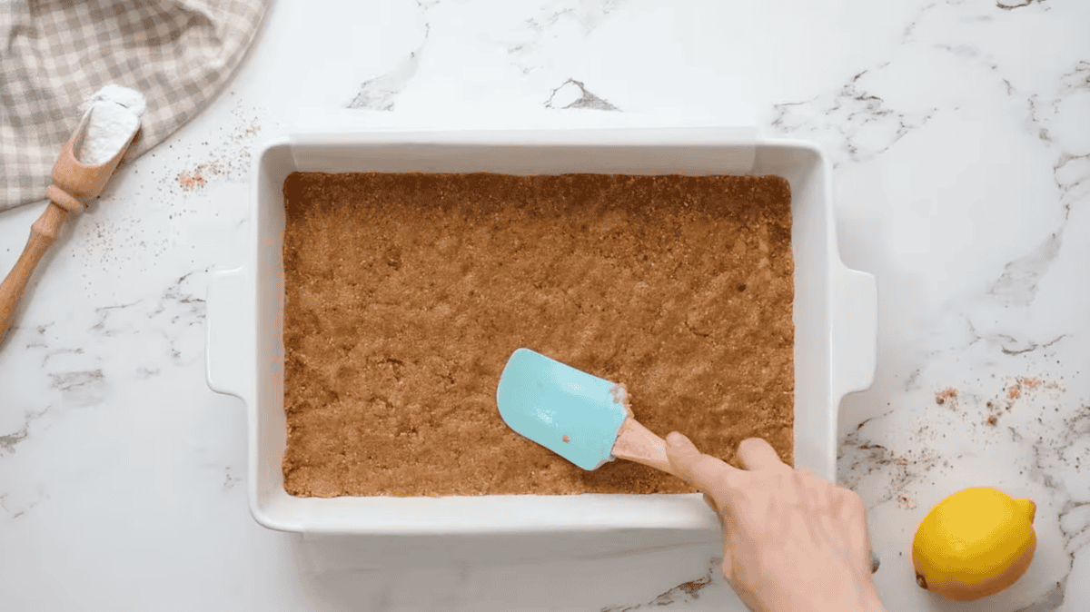 pressing graham cracker crust into a baking pan with a rubber spatula.