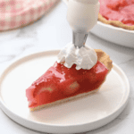 a slice of strawberry jello pie on a white plate with whipped cream.