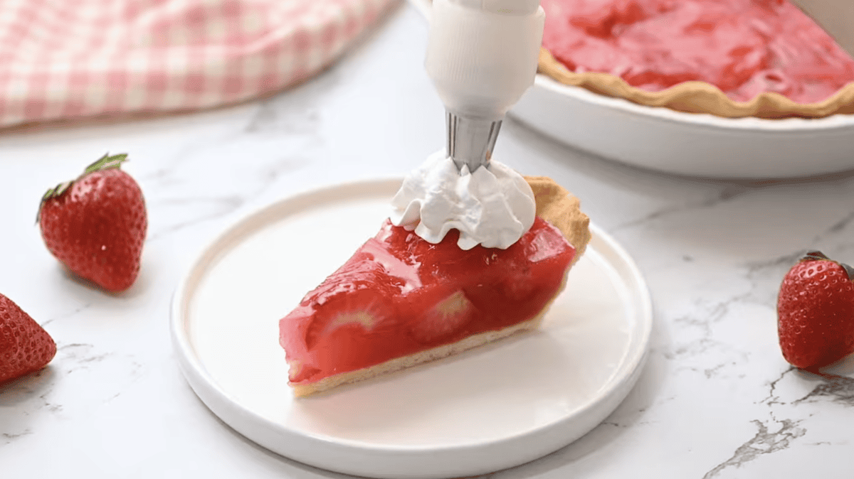 a slice of strawberry jello pie on a white plate with whipped cream.