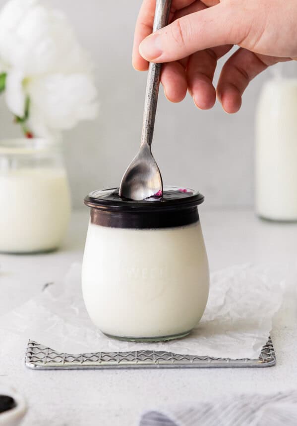 plunging a spoon into vanilla panna cotta in a jar with chocolate on top.